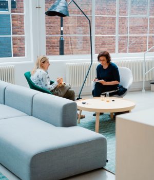 two woman sits on sofa chairs inside house